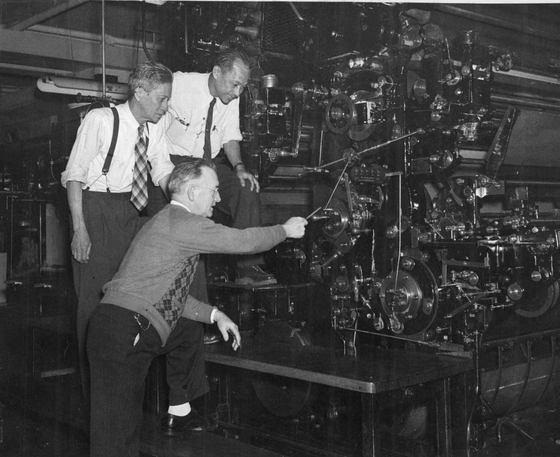 Three men stand around a large machine.