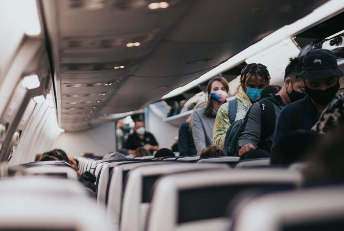 people wearing masks board an airplane